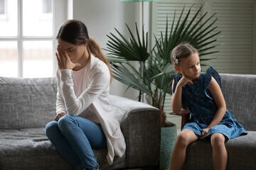 Obraz premium Unhappy young Caucasian mother and small teen daughter sit separately back to back after family quarrel. Upset sad mom and little girl child avoid ignore talking after fight. Generation gap concept.