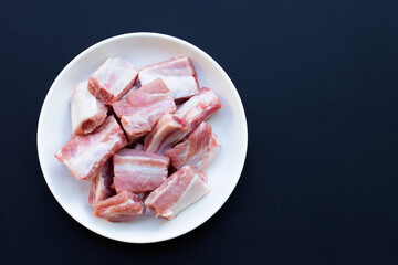 Raw pork ribs in white plate on dark background.