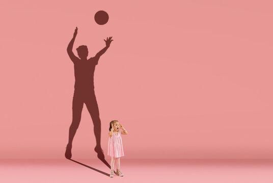 Childhood and dream about big and famous future. Conceptual image with little girl and shadow of female volleyball player on coral pink wall, background.