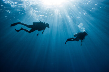 Two Scuba Divers on the blue ocean with sunlights rays over the sea.