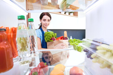 Portrait of female standing near open fridge full of healthy food, vegetables and fruits