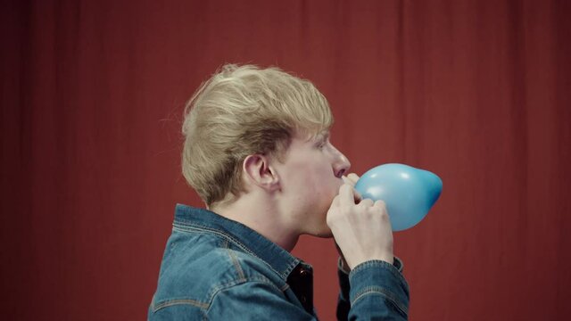 Happy birthday british Cute man blowing up Colorful blue Balloon, positive male portrait, emotional blonde student posing in studio.
