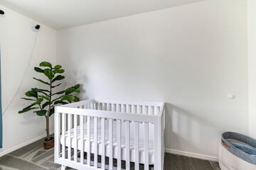 White nursery room with white crib, camera monitor and gray carpet floor