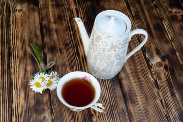 Cup of chamomile tea and chamomile flowers on wooden background. Close-up.