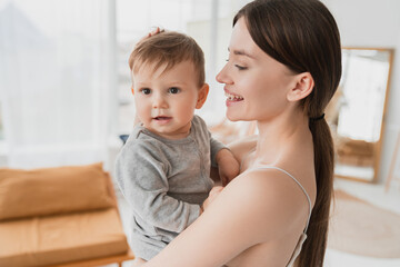 Little caucasian baby toddler infant sitting on mother`s hands, young single mother embracing her son daughter with love and care. Motherhood and postnatal period. Maternity leave concept