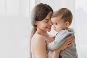 Cheerful young single mother hugging embracing little small son daughter baby newborn infant...