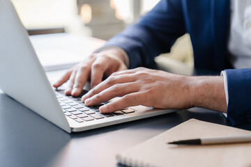 Cropped close up image of businessman`s hands typing working on laptop at home office. Freelancer, remote occupation,tutor, student e-learning concept
