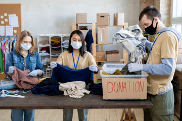 Three volunteers in masks and gloves sorting donation clothes