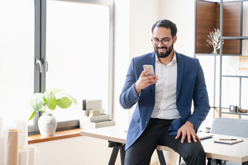 Handsome Middle Eastern businessman freelancer CEO boss having work break using smart phone for...