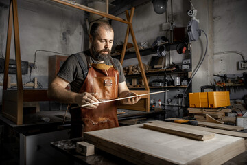 Naklejka na ściany i meble Brutal master carpenter prepares wooden blanks for work in workshop