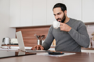 Confident young businessman tutor freelancer using laptop checking e-mails, working online, paying...