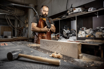 Fototapeta na wymiar Brutal master carpenter in an apron adjusts plane in workshop