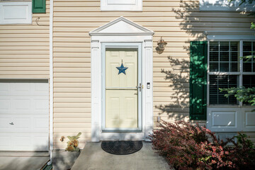 Exterior of a front door with blue star, doorbell, vinyl siding walls and windows