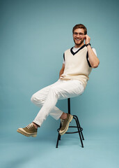 Feeling comfortable. Joyful positive young man sitting on a stool and smiling isolated on blue.