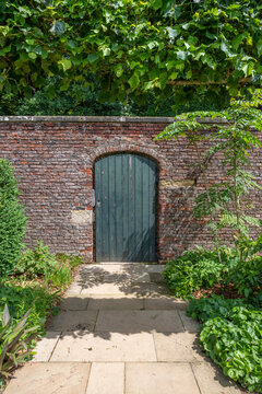 A green walled garden door in a red brick wall with a slabed footpath