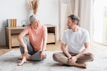 Healthy mature couple family spouses sitting on the floor after fitness exercises talking...