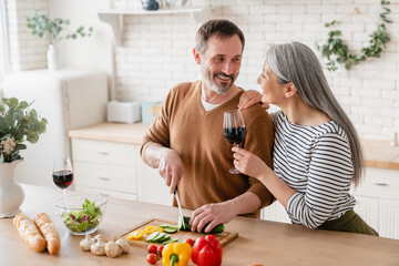 Relaxed mature middle-aged couple cooking together romantic dinner for date at home in the kitchen,...