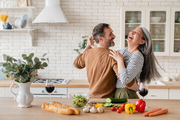 Happy cheerful middle-aged mature couple family parents dancing together in the kitchen, preparing...