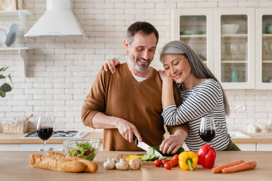 Happy Middle-aged Family Cooking Vegetable Salad In The Kitchen At Home Together. Mature Wife Helping Prepare Food Meal Her Husband. Vegetarian Healthy Eating