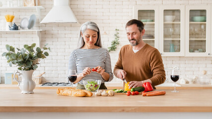 Cheerful mature couple middle-aged family wife and husband cooking vegetable vegetarian salad...