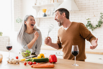 Happy mature caucasian middle-aged couple family wife and husband cooking vegetable salad in the...