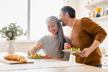 Loving mature husband kissing his middle-aged wife during breakfast at home in the kitchen. Mature...