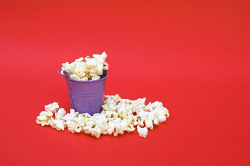 The fresh popcorn in a small decorative iron bucket on a red background.