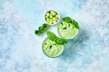 Cucumber Gazpacho - cold summer soup with basil in glasses on light background. Top view Flat lay.