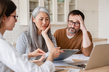 Financial advisor lawyer consulting mature middle-aged couple showing them debts, bunkruptcy,...