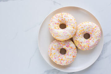 Donuts on a white plate on white marble surface. Photo flat lay, top view.