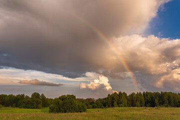 Fototapeta na wymiar Rainbow over stormy sky. Rural landscape with rainbow over dark stormy sky in a countryside at summer day.