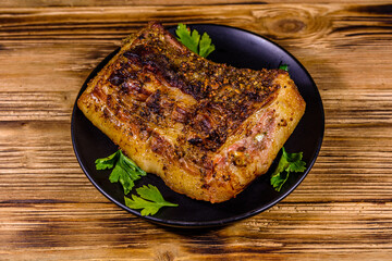 Baked piece of pork belly and parsley on a black plate