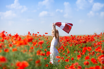 Blond girl holding flag of Latvia in the poppy field. Declaration of Independence Day. Ligo. Proclamation of the Republic of Latvia. Travel and learn latvian language concept. - obrazy, fototapety, plakaty