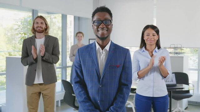 African young boss smiling at camera with diverse team applauding on background