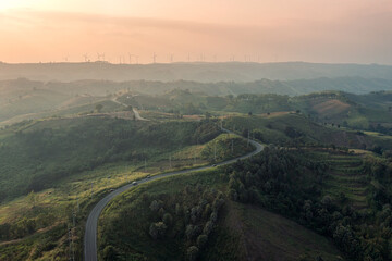 Fototapeta na wymiar Aerial view of Curved highway on green hill and wind turbine on peak at sunset in countryside