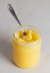 Indian ghee clarified butter desi in the open glass jar with a spoon on neutral grey background