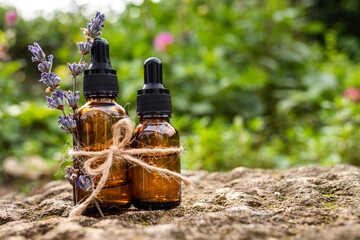Cosmetic bottles made of brown glass with lavender oil on a nature background.