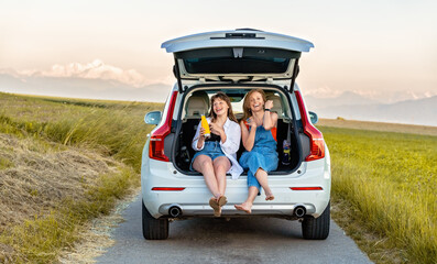 Mother and teenager daughter having fun enjoying their road trip in countryside sitting in open car...