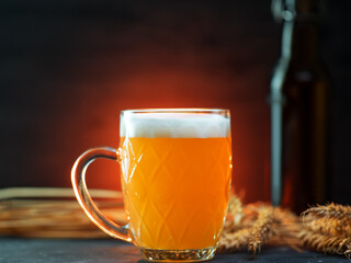 A mug of traditional wheat beer on a dark table, a bottle of bugel. Wheat ears, colorful backlight
