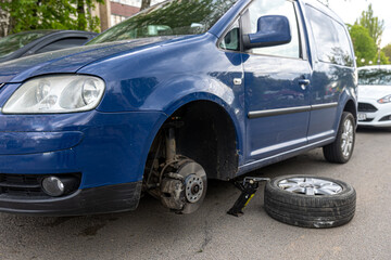 A broken wheel is standing next to the car.