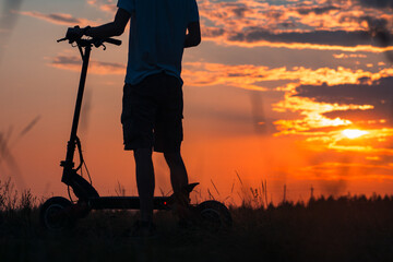 The feeling and concept of freedom. Riding an electric scooter. A young man on a scooter enjoys the sunset