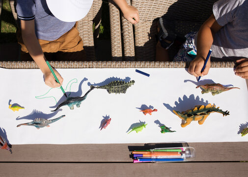 children draw contrasting shadows from toy dinosaurs with felt-tip pen. ideas for children's creativity. Interesting activities for children at home and in kindergarten. View from above