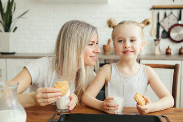 Obraz na płótnie Canvas Cute little girl and mom eating freshly baked cookies with milk
