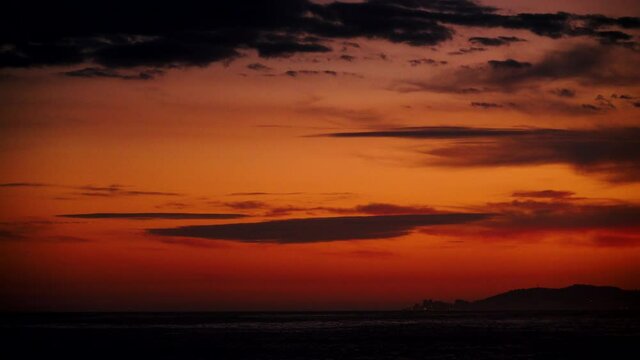 Time lapse of clouds moving over sea. Red orange sky after sunset, night is falling. Nature, coastal landscape. Capi Corb, Mediterranean coast of Spain.