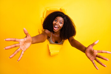 Photo of young excited afro girl happy smile open arms hug cuddle embrace torn paper hole isolated over yellow color background