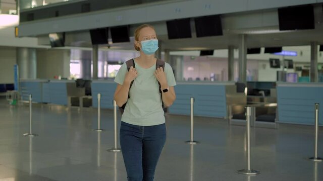 Woman in mask at empty airport at check in in coronavirus quarantine isolation, returning home, flight cancellation, pandemic infection worldwide spread, travel restrictions and border shutdown