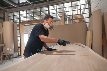 Man in respirator mask painting wooden planks at workshop. Craftsman modern furniture factory paint