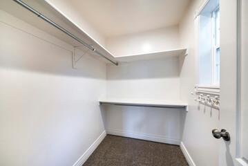 Walk in closet with dark brown carpet flooring and wall mounted shelves and hooks