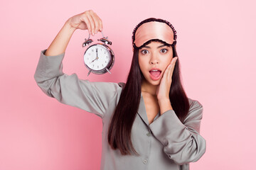 Portrait of beautiful trendy amazed stunned girl holding clock call awake isolated over pink pastel color background