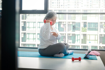 Asian elderly woman sit exercise at home Do yoga poses according to an online fitness teacher via...